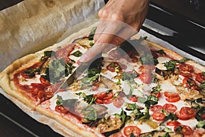 Woman cutting by knife rectangular shape and thick hand made romana`s pizza traditional italian pizza margherita closeup