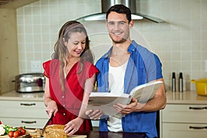 Woman cutting loaf of bread and man checking recipe book