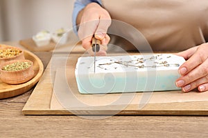 Woman cutting natural handmade soap on wooden table