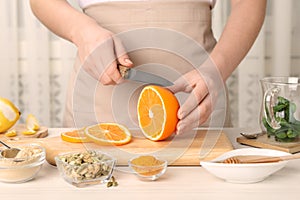 Woman cutting orange for immunity boosting drink at white wooden table