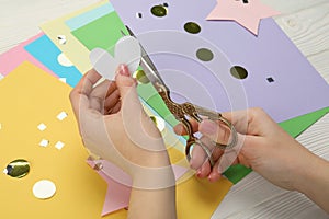 Woman cutting paper heart with scissors at white wooden table, closeup