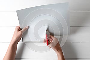 Woman cutting paper with scissors at white wooden background, top view