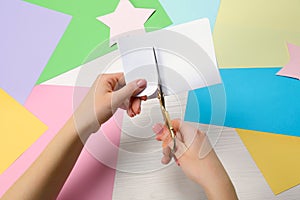 Woman cutting paper with scissors at white wooden table, top view