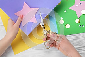 Woman cutting paper star with scissors at white wooden table, top view