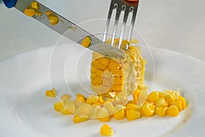 Woman cutting piece of baked corn on plate on kitchen at home.