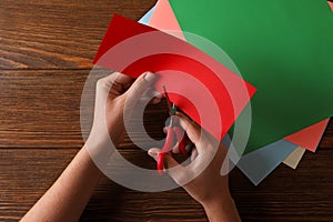 Woman cutting red paper with scissors at wooden background, top view