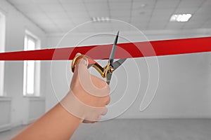 Woman cutting red ribbon on blurred background