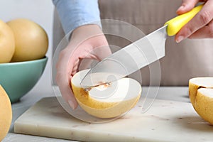 Woman cutting ripe apple pear at table, closeup
