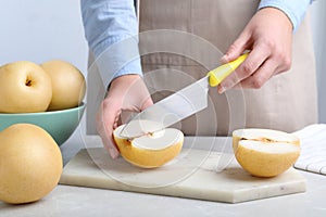 Woman cutting ripe apple pear at table, closeup
