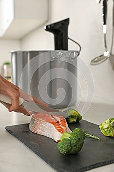 Woman cutting salmon near pot with sous vide cooker in kitchen. Thermal immersion circulator