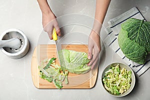 Woman cutting savoy cabbage on wooden board at table