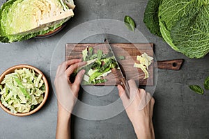 Woman cutting savoy cabbage on wooden board at table