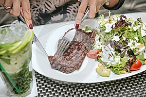 Woman Cutting Steak With Knife and Fork at Restaurant Table