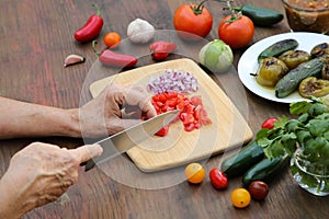 Woman cutting tomato for salsa sauce at wooden table, closeup