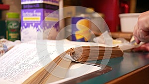 Woman cutting up butter while reading an old cookbook or recipe book in kitchen