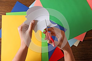 Woman cutting white paper with scissors at wooden table, top view