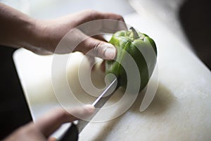 Woman cutting whole green capsicum with a knife on a chopping board in an Indian kitchen
