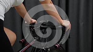 Woman cycling indoors close up view hands on handlebars with cycling computer and wheel. Indoor training on smart bike trainer.