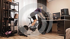 Woman is cycling on smart bicycle trainer. Indoor cycling. Female cyclist is doing fitness workout on exercise bike. Athlete is pe