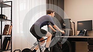 Woman is cycling on stationary bicycle. Indoor cycling. Home sport activity. Female cyclist is training on smart bike trainer. Ath