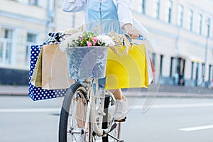 Woman is cycling on white bicycle with packages on handlebars