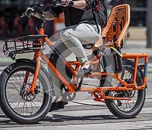 Woman cyclist amateur rides a powerful electric bike with an additional seat for children moves along the city street