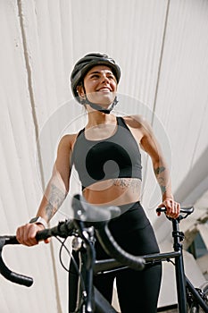 Woman cyclist in protective gear standing with her bike while training outdoors and looks away