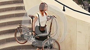 Woman cyclist walking down stairs and holding bicycle in arms. Woman bike city