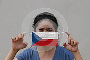 A woman with Czech Republic flag on hygienic mask in her hand and lifted up the front face on beige color background. Tiny