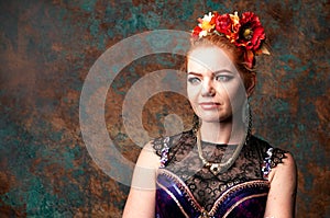 Woman in dance costume with black lace in red circlet of flowers looking away in front of teal and orange background