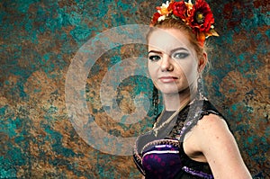 Woman in dance costume with black lace in red circlet of flowers looking at camera in front of teal and orange background