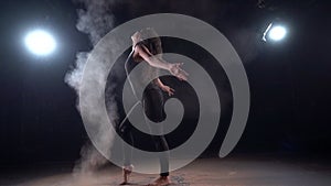 Woman dancer is making clouds of dust or powder by movement of hair, silhouette in darkness