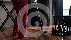 A woman dances with a vacuum cleaner. A young woman cleans her house, listens to music and expresses positive emotions -