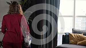 A woman dances with a vacuum cleaner. A young woman cleans her house, listens to music and expresses positive emotions -