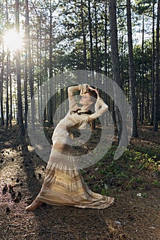 A woman is dancing in a dress in nature, leaning back among the coniferous trees in the forest