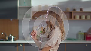 Woman dancing on kitchen. Lady gesturing with whisker in hand at kitchen