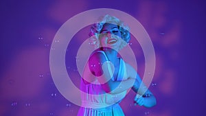 Woman dancing surrounded by soap bubbles, sending air kisses. Woman in the image of Marilyn Monroe on a pink background