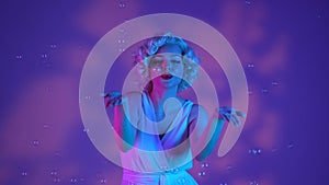 Woman dancing surrounded by soap bubbles, sending air kisses. Woman in the image of Marilyn Monroe on a pink background