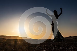 Woman dancing to the famous Arab belly dance. With sunset in the arid desert plain of Namibe. Africa. Angola