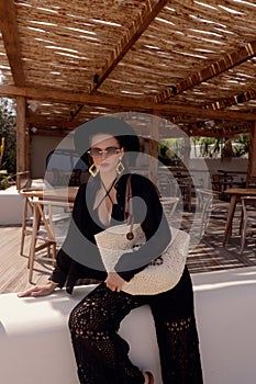 woman with dark hair in elegant clothes with accessories posing in summer beach club