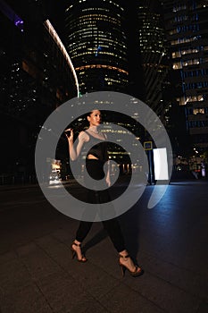 woman with dark hair in elegant dress and accessories walks around the night city with skyscrapers in the background