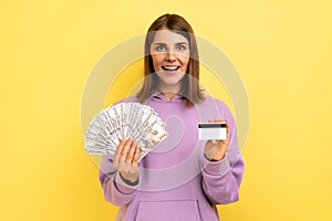 Woman with dark hair holding fan of dollars banknotes and credit card, earning money, banking.