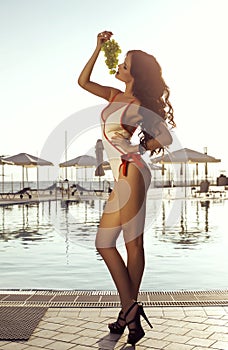 woman with dark hair in swimsuit posing with bunch of grapes
