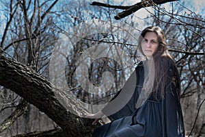 Woman with dark long hair in black robes hanging on tree branches in the middle of a swamp. Halloween and Gothic concept.