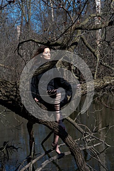 Woman with dark long hair in black robes hanging on tree branches in the middle of a swamp. Halloween and Gothic concept.