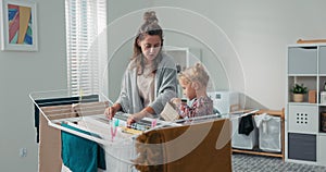 A woman and daughter are doing household chores, putting clean clothes out of the washing machine on the dryer, a little