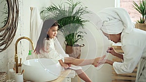 Woman and daughter paint toe in bathroom Spbd. Feminine asian mother and girl in bathrobe do beauty