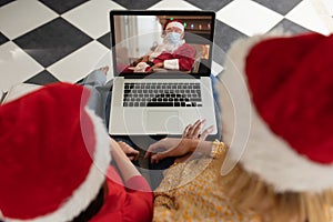 Woman and daughter in Santa hats having a video chat with Santa Claus in face mask on laptop