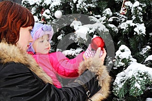 Woman with daughter stands near green tree