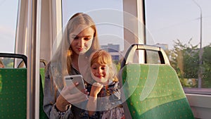 Woman and daughter using mobile phone internet social network application, traveling by bus or tram